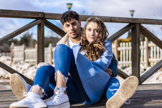 Young couple sitting on an old wooden bridge, looking at the camera